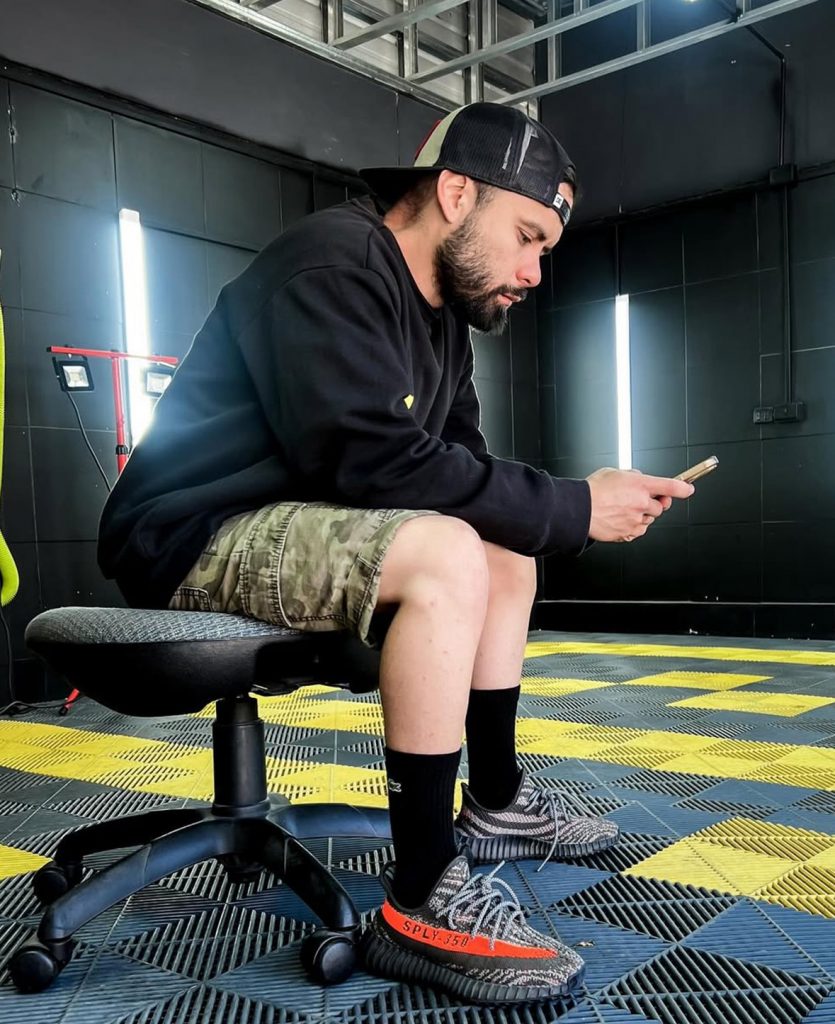 HOMBRE SENTADO EN UN TALLER DE DETALLADO AUTOMOTRIZ REVISANDO LA AGENDA EN SU TELEFONO CELULAR